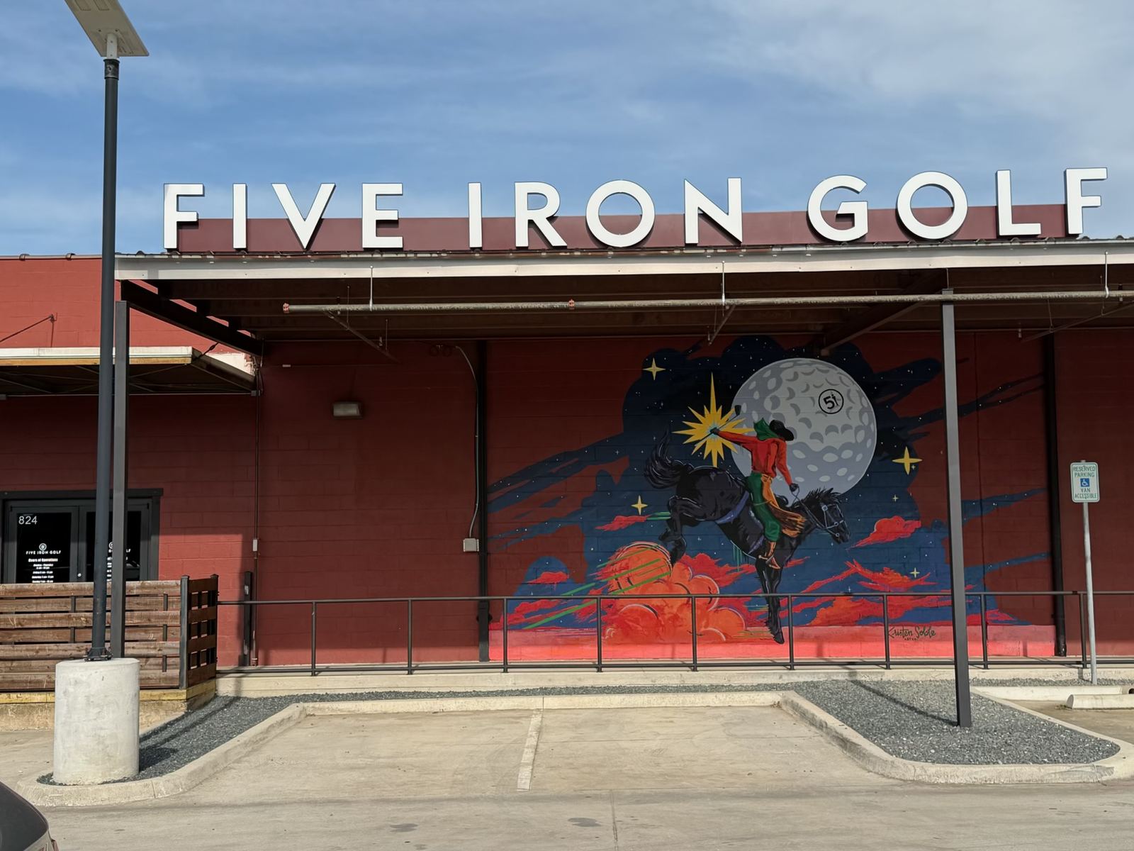 The Five Iron Golf Fort Worth building on W. Daggett Ave — red brick with rooftop FIVE IRON GOLF lettering and a mural of a cowboy riding toward a golf-ball moon.